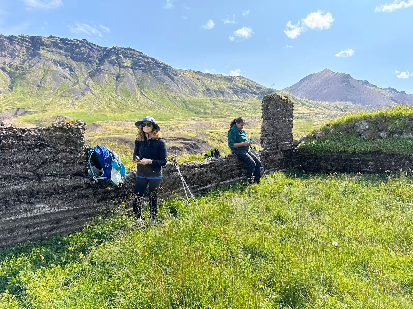 Two hikers resting at ancient stone ruins surrounded by lush green valleys on a 5-day East Iceland hiking tour