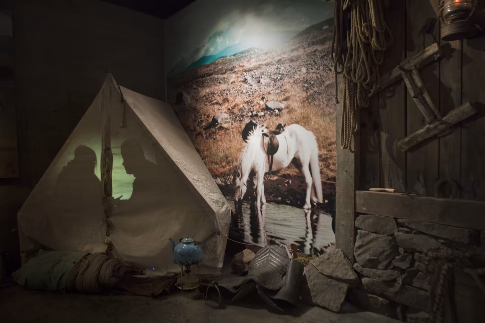 Museum exhibit with tent, silhouettes, and white horses at water in East Iceland history display