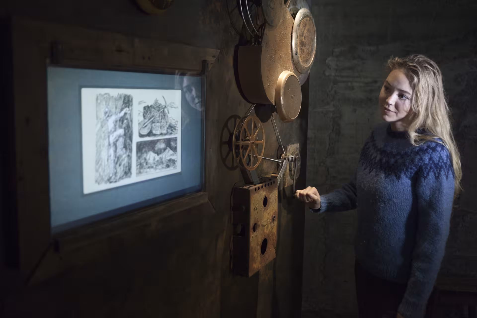 Woman in Icelandic sweater operating vintage film projector showing historical drawings in East Iceland museum