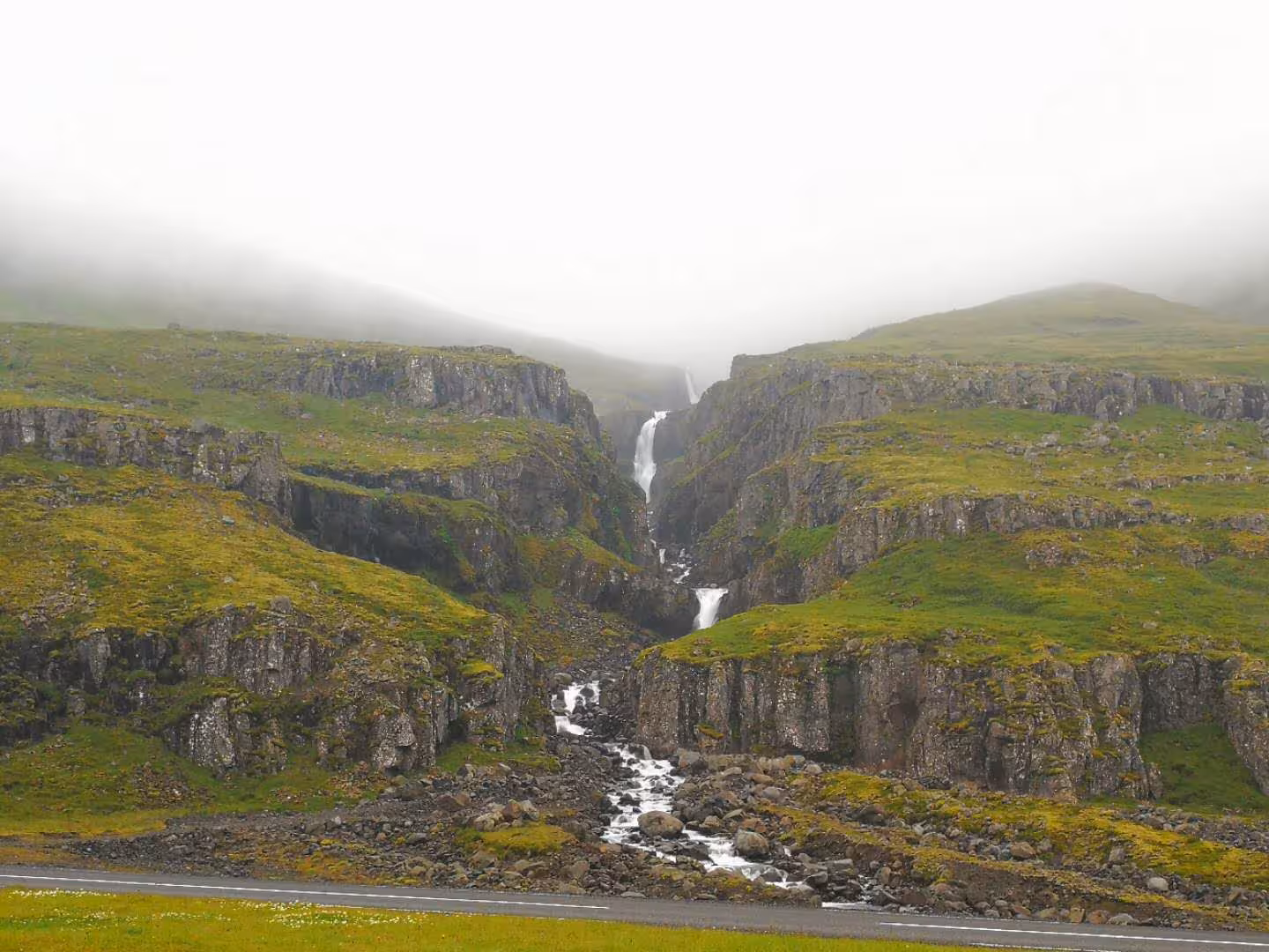 Misty canyon waterfall cascading through green moss-covered basalt cliffs in the Eastfjords Iceland