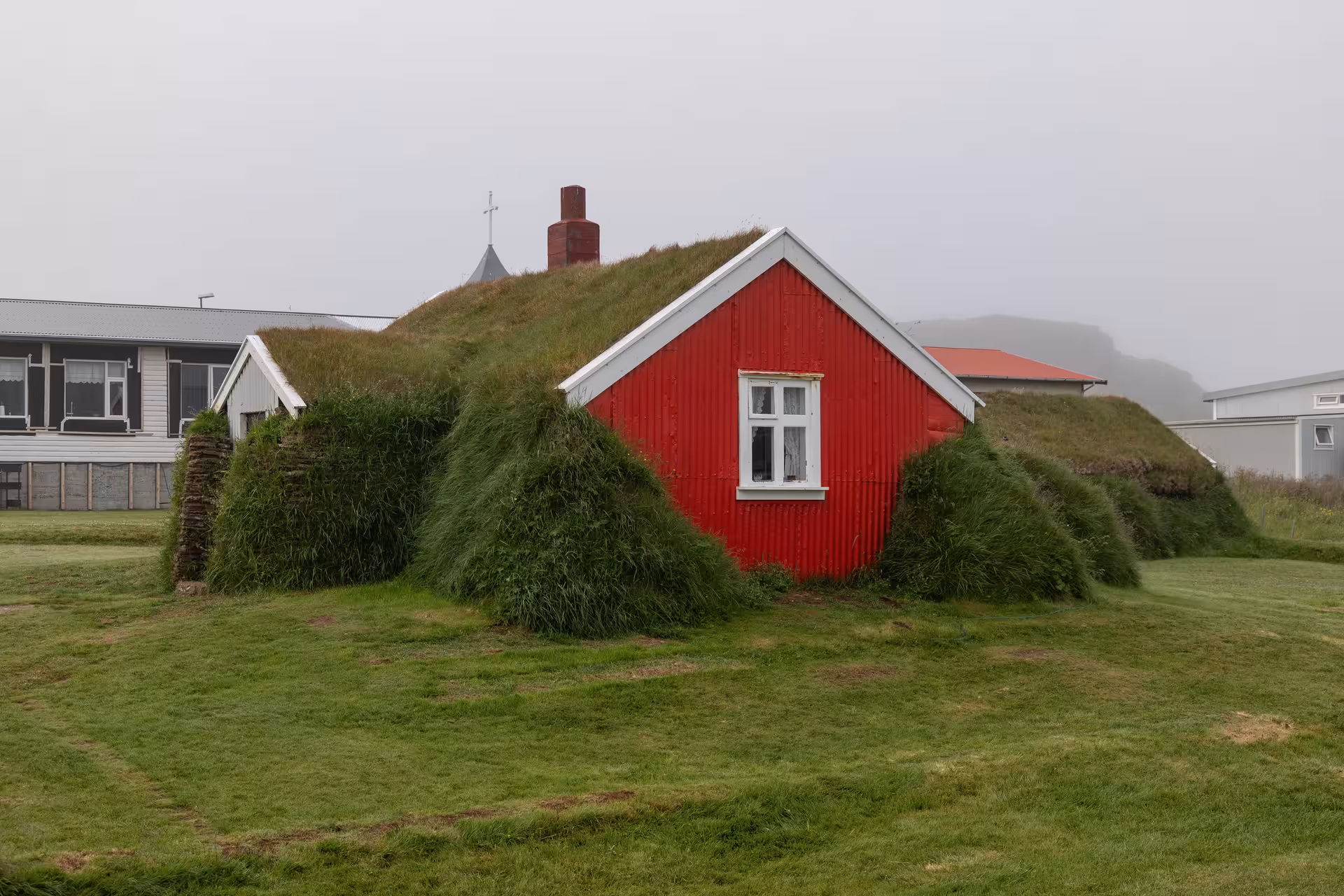 Traditional red turf-roofed house covered in green grass in the Eastfjords of Iceland