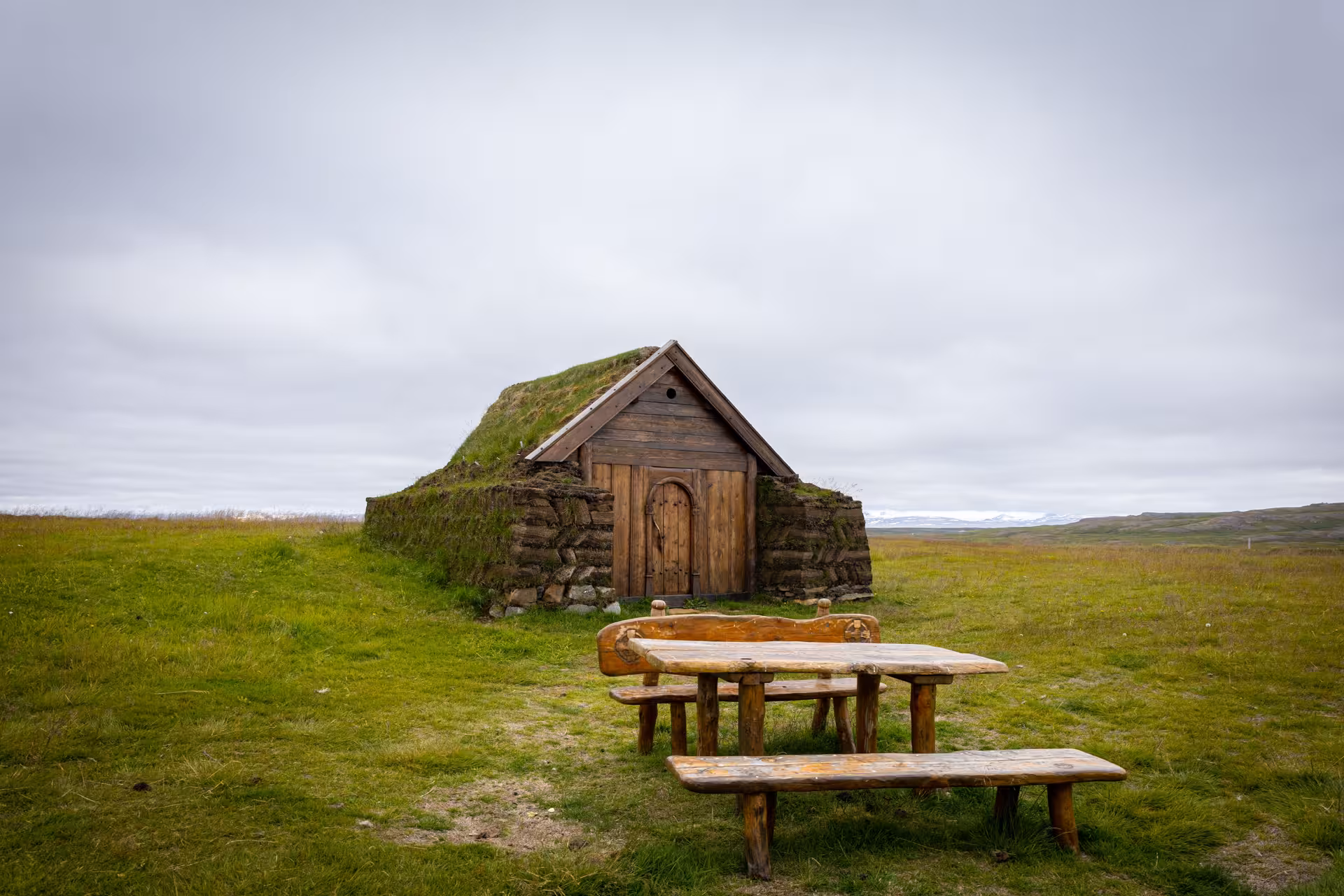 Traditional Icelandic turf house with grass roof and wooden door on open green meadow in the Eastfjords