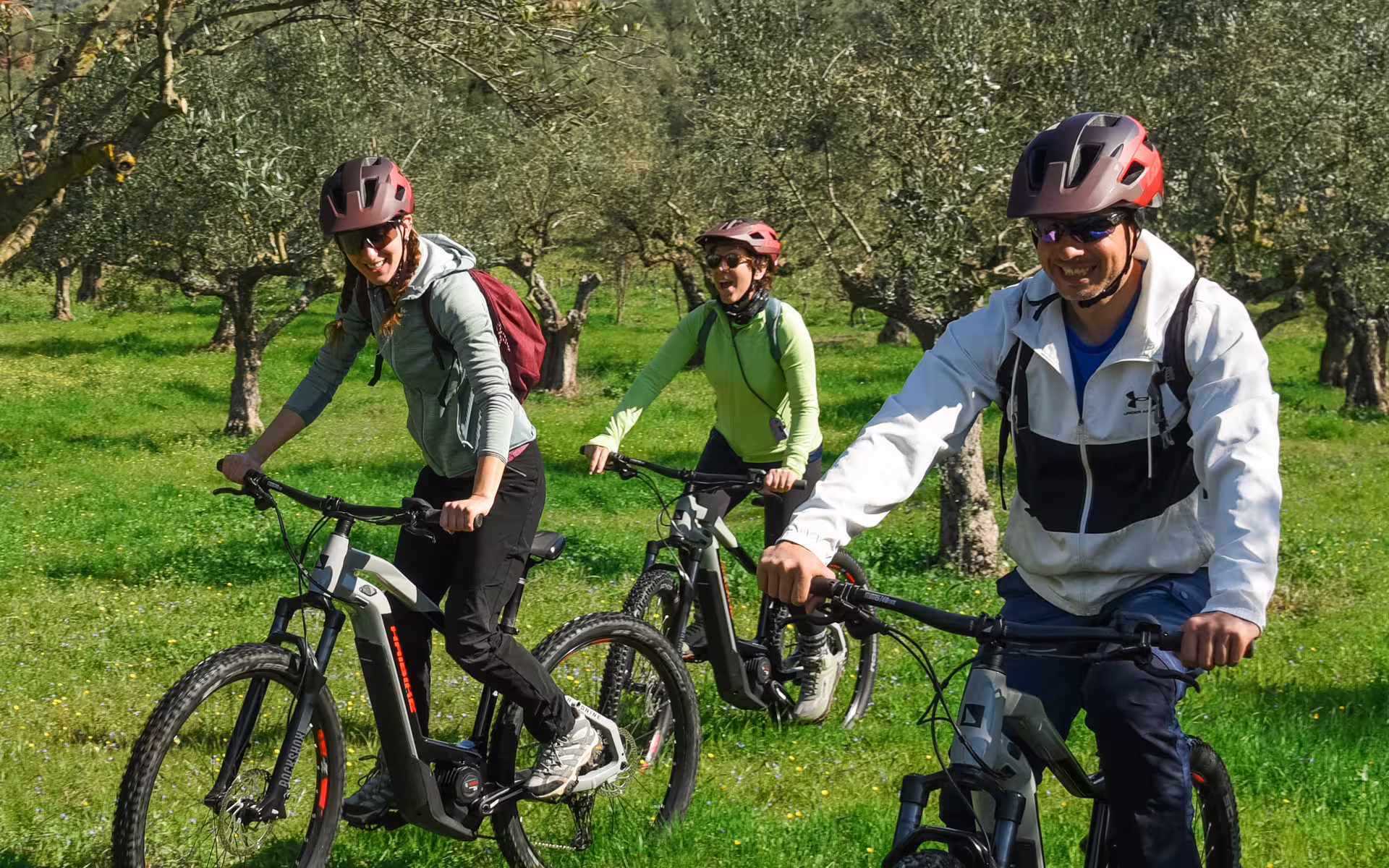 Smiling group on e-bikes riding through olive groves in Messinia, Greece on the Ancient Messene Way tour