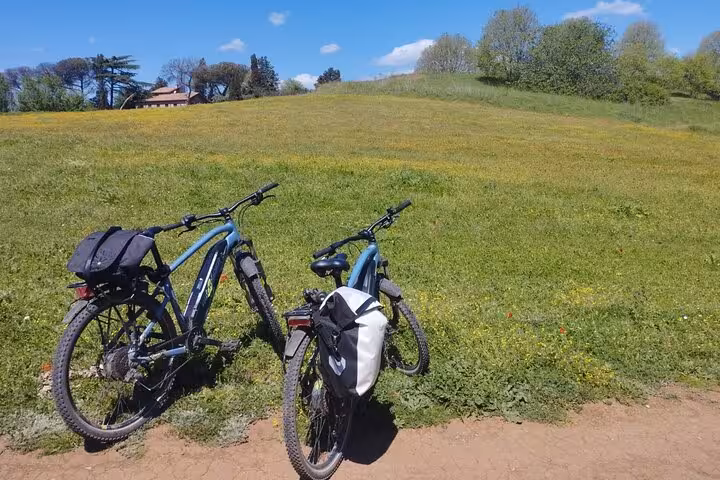 Two e-bikes resting on a grassy hill along the scenic Appian Way, perfect for exploring Rome's nature and history.
