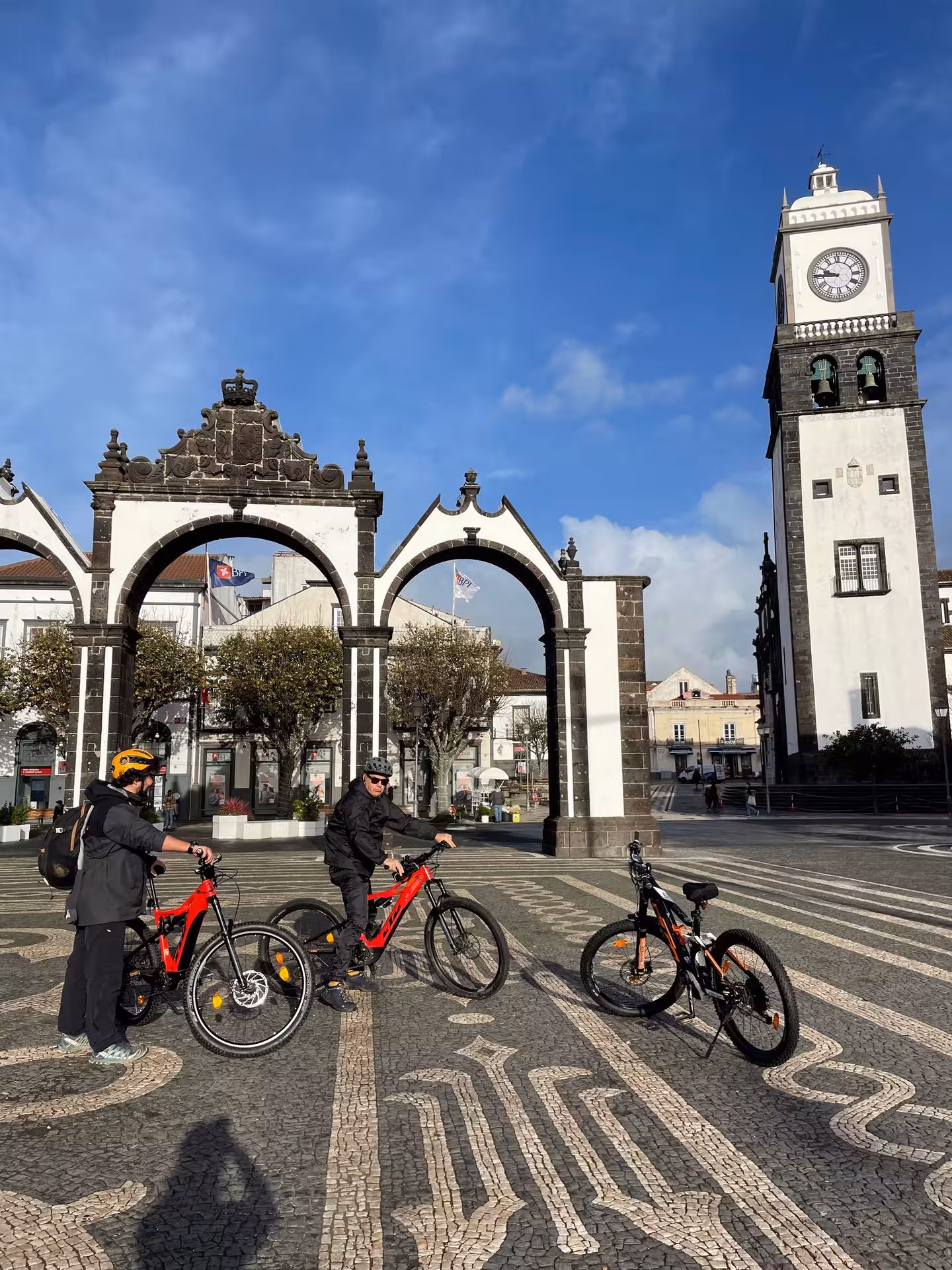 Guided e-bike city tour stopping by historic arches and clock tower in Ponta Delgada, Azores on a sunny morning