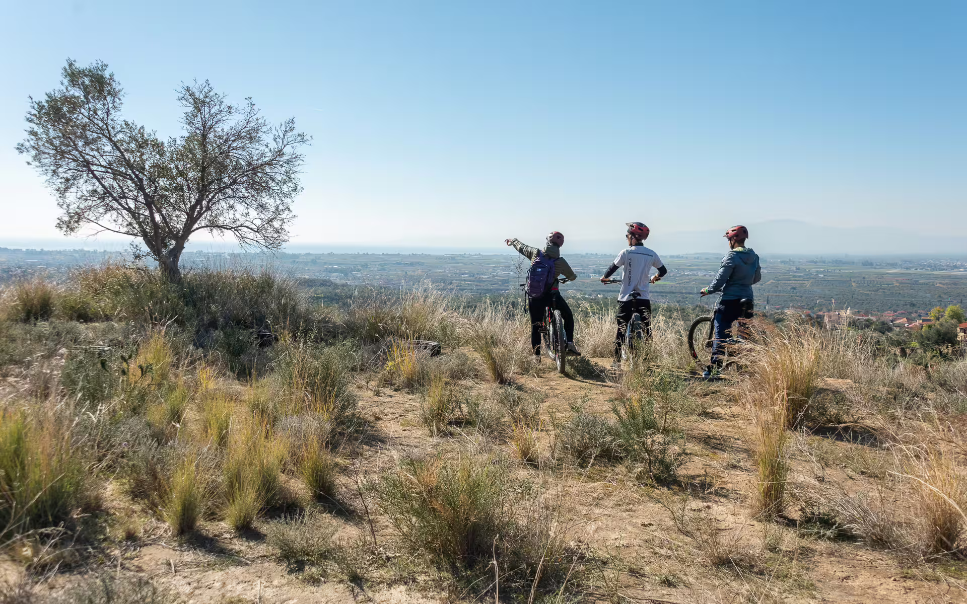 E-bike riders on a Kalamata olive route viewpoint, overlooking Messinia plains and distant sea in Greece