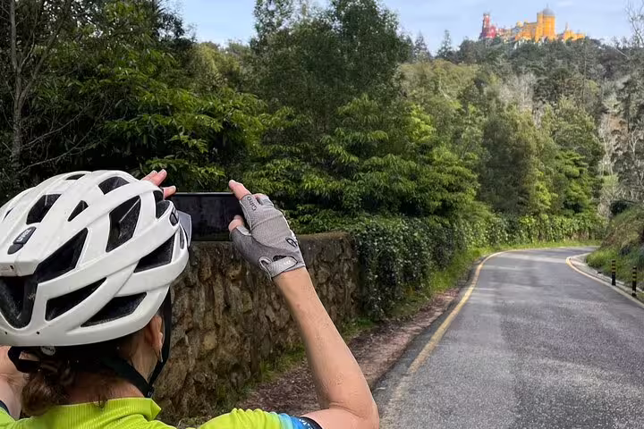 Cyclist capturing a stunning view of Pena Palace while exploring the lush trails of Cascais and Sintra on an e-bike.