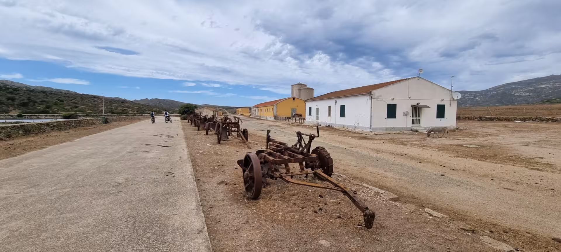 E-bike riders explore historic Asinara village with rustic buildings and old machinery near Porto Torres.