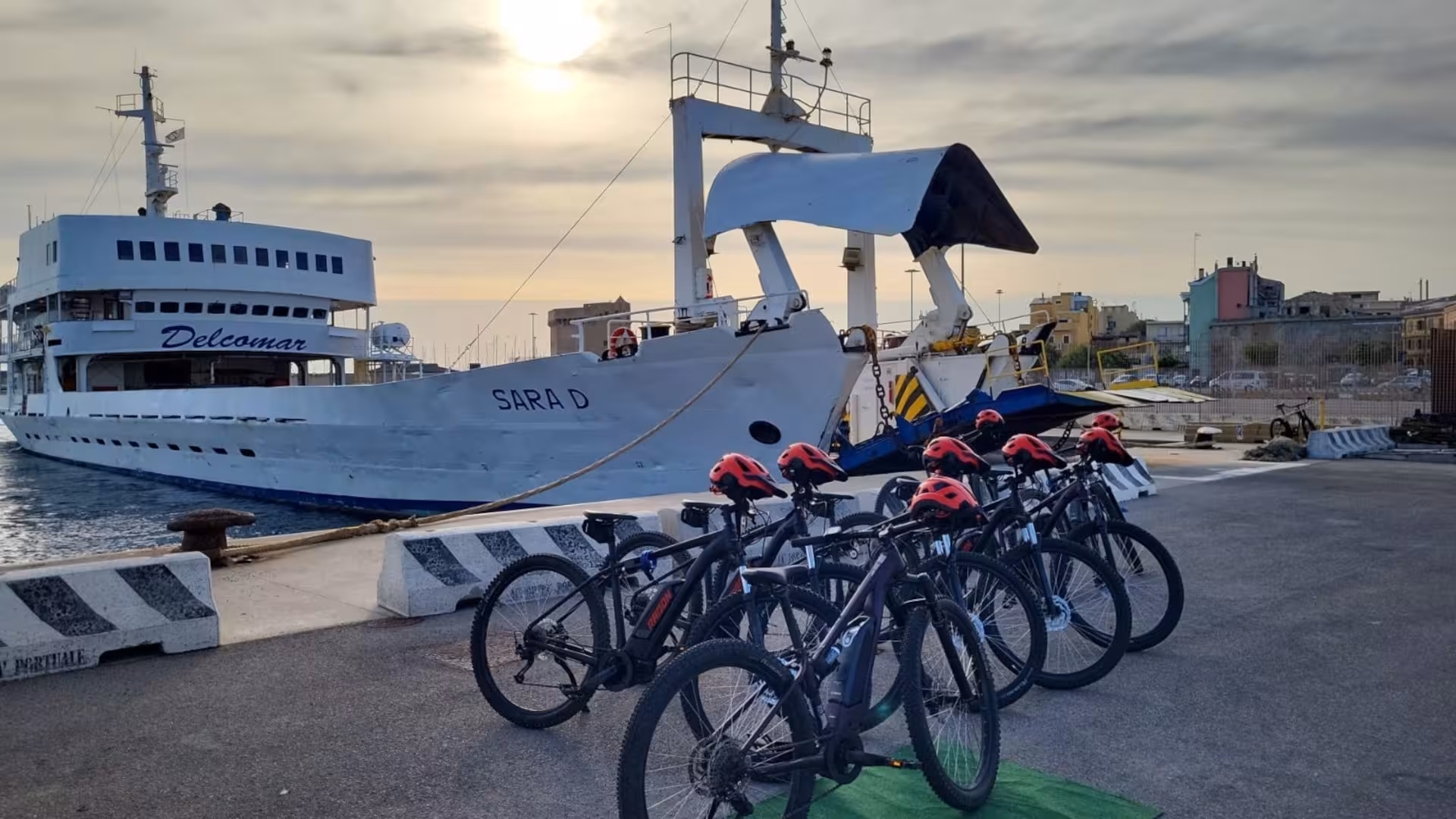 E-bikes with helmets ready at Porto Torres pier with a ferry background for Asinara island exploration tour.