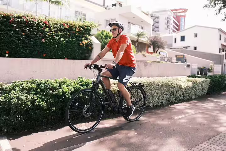 Cyclist enjoying an e-bike road tour from Cabo Girão to Funchal, passing scenic urban landscapes and lush greenery.