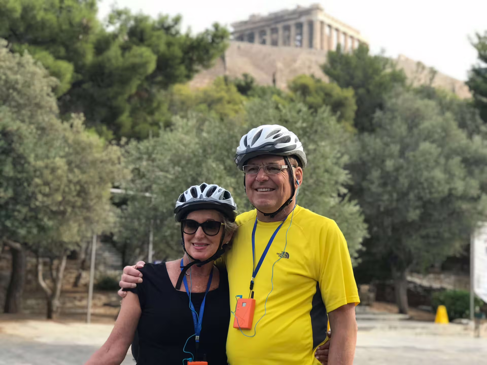 Couple enjoying e-bike tour in Athens with the Acropolis in the background, perfect for cultural exploration.