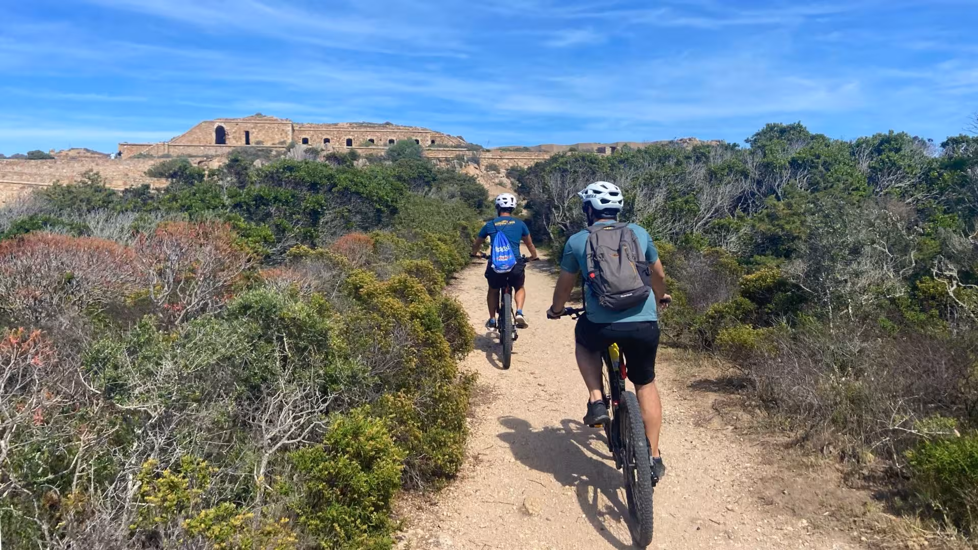 Cyclists on an e-bike tour exploring trails towards historic sites in Caprera and La Maddalena.