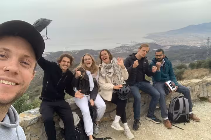 Happy e-bike tour group at Montes de Malaga viewpoint with helmets and Malaga coastline in the background