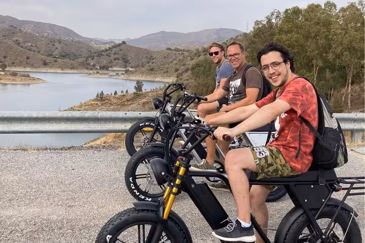 Friends on off-road e-fat bikes at a Malaga mountain reservoir viewpoint during Montes e-bike tour adventure