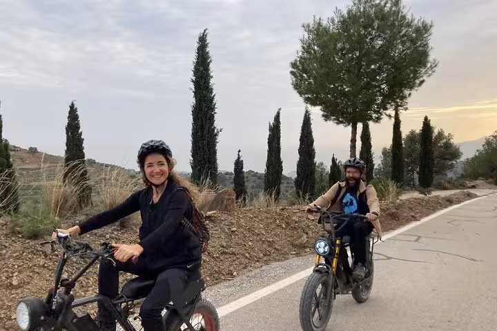 Guided e-fat bike tour in Montes de Málaga with cyclists on a scenic road lined with cypress trees