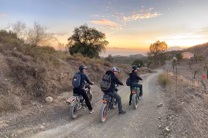 Group riding off-road e-fat bikes on a gravel trail at sunset in the Montes de Malaga on guided e-bike tour