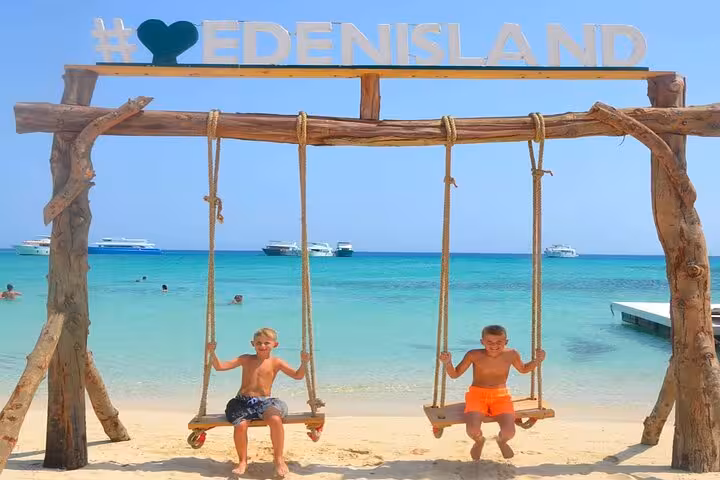 Eden Island beach swing photo spot on Hurghada day trip, turquoise Red Sea lagoon and boats behind
