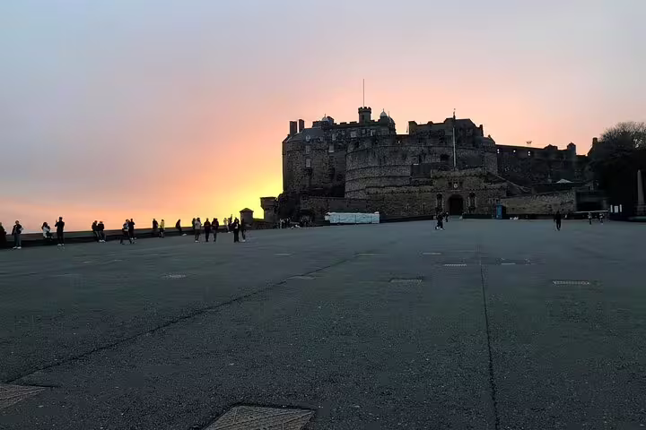 Edinburgh Castle silhouetted against a vivid orange sunset sky with visitors on the esplanade