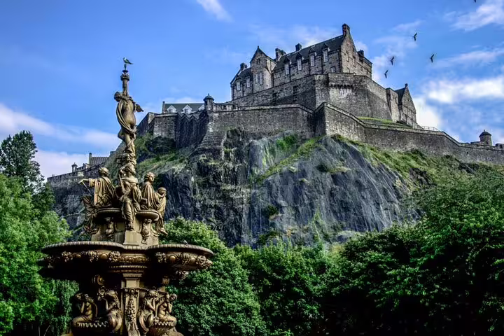 Edinburgh Castle perched on volcanic rock with ornate Ross Fountain and lush gardens in foreground