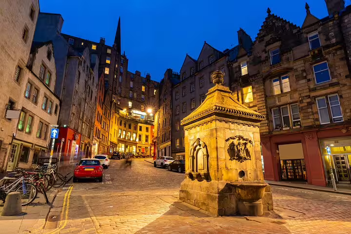Historic cobblestone street in Edinburgh Old Town at night with stone fountain and medieval buildings