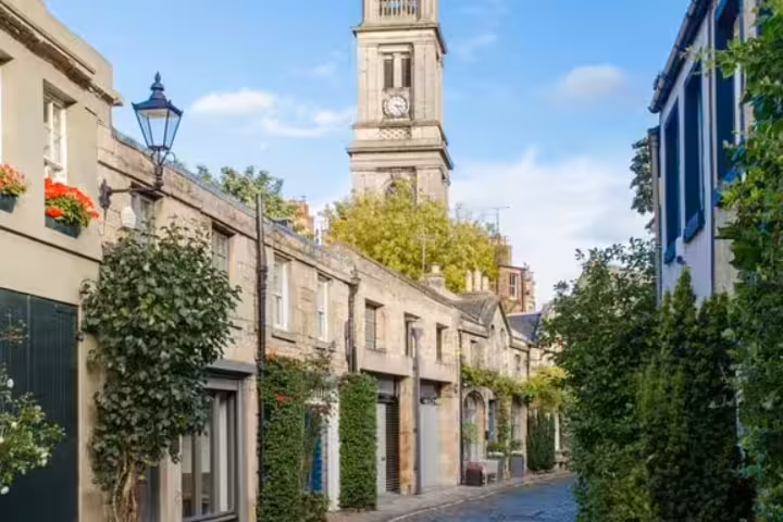Charming cobblestone mews street with stone buildings, ivy, gas lamp, and church clock tower in Edinburgh
