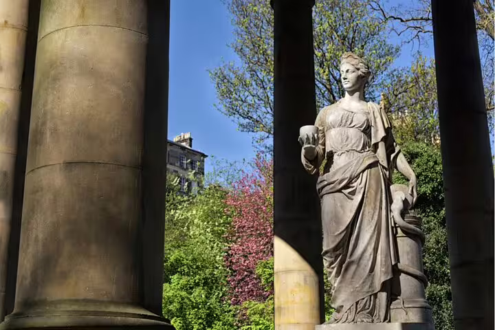 Classical stone statue of a woman holding a vessel between ornate columns in Edinburgh gardens