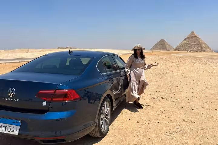 Tourist enjoying a scenic view of the Pyramids of Giza with a parked car during the unique Egypt in 11 days tour.