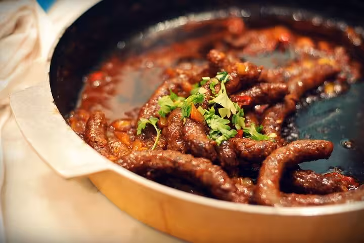 Sizzling Egyptian sausages in a rich, spicy sauce, topped with fresh herbs, perfect for an authentic Cairo food tour.