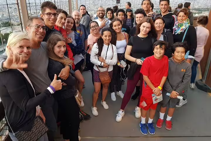 Large tour group smiling together on Eiffel Tower observation deck with Paris cityscape in background