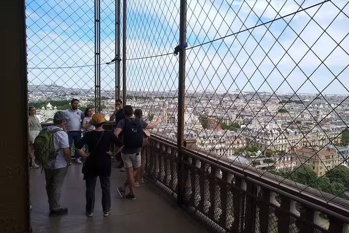 Tourists viewing Paris cityscape from Eiffel Tower observation deck with safety mesh fencing