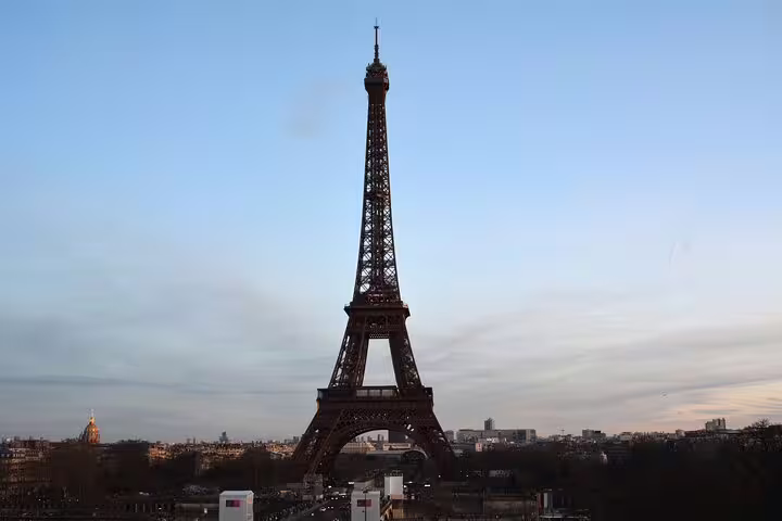 Eiffel Tower standing tall against a blue dusk sky with Paris cityscape in the background