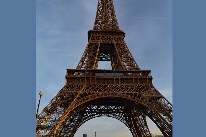Upward view of the Eiffel Tower iron lattice structure against a blue sky in Paris