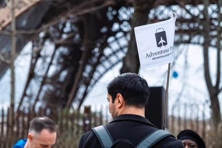 Tour guide holding Adventour Paris flag near the base of the Eiffel Tower with visitors