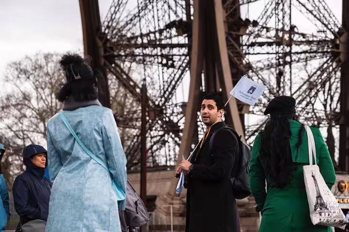 Tour guide holding flag leads group of tourists at the base of the Eiffel Tower in Paris