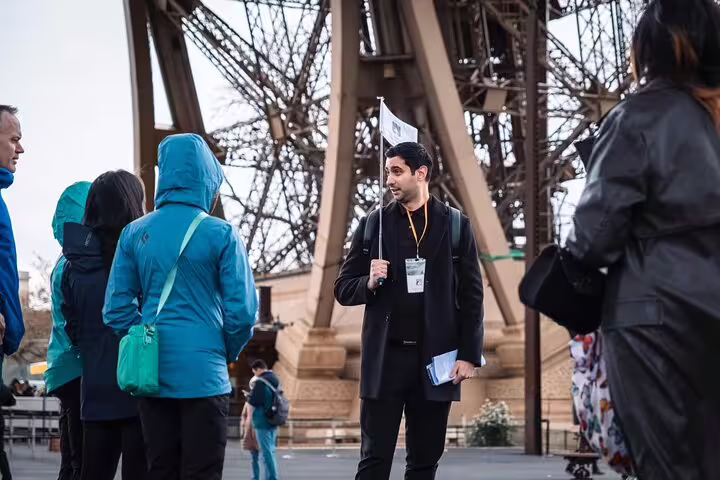 Tour guide holding flag leads group at base of Eiffel Tower in Paris