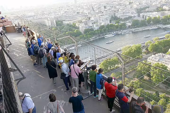 Tourists on Eiffel Tower observation deck with panoramic view of Paris and Seine River below