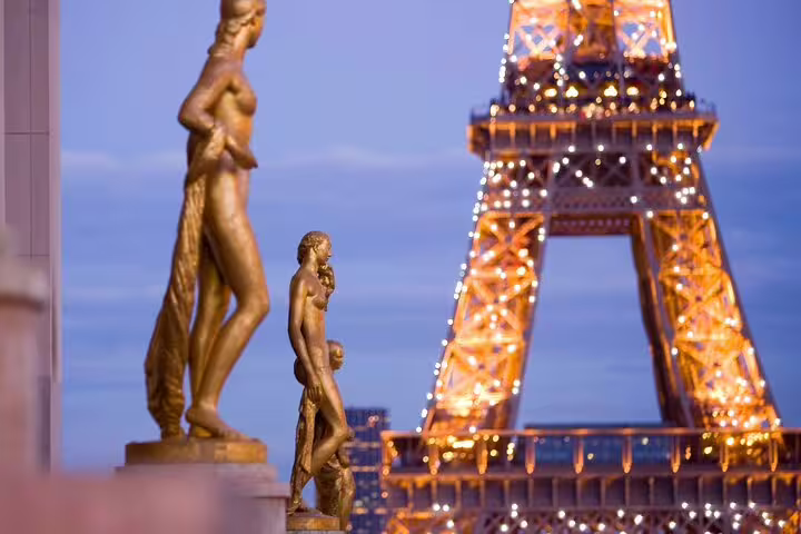 Golden statues at Trocadéro with illuminated Eiffel Tower glowing at dusk in Paris