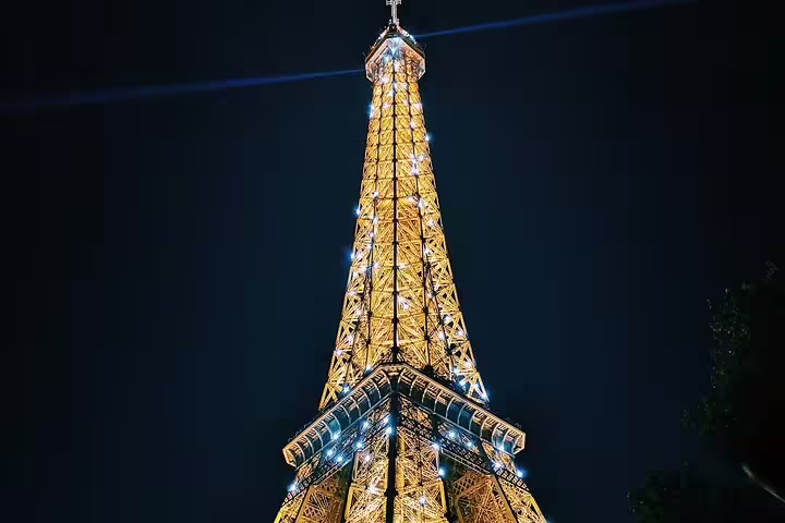 Eiffel Tower illuminated with golden lights and sparkling white lights at night, viewed from below
