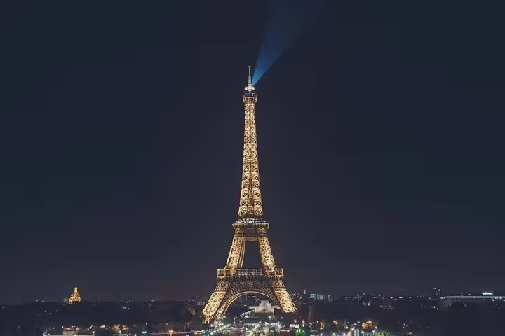Eiffel Tower illuminated at night with golden lights and blue beacon, Paris city skyline in background
