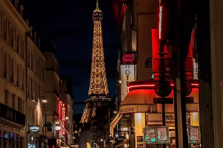 Eiffel Tower illuminated at night viewed from a bustling Saint Germain street in Paris