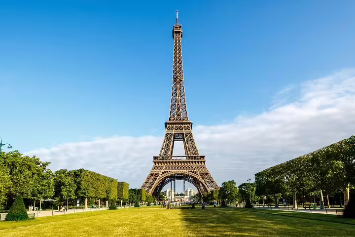 Eiffel Tower rising above green Champ de Mars park under clear blue sky, Paris