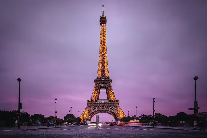 Eiffel Tower illuminated at dusk with purple sky, viewed from Champ de Mars in Paris