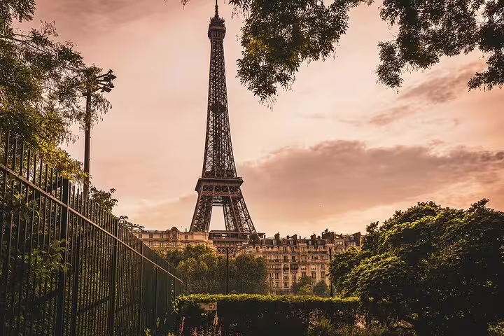 Eiffel Tower rising above lush green trees and Haussmann buildings at golden sunset in Paris