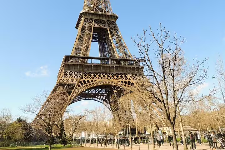 Eiffel Tower viewed from ground level with bare trees and visitors in Paris on a clear day