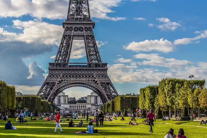 Eiffel Tower with visitors relaxing on green lawns of Champ de Mars on a sunny day in Paris