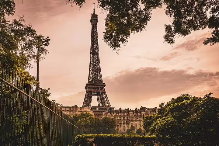 Eiffel Tower rising above Parisian buildings and lush trees at golden sunset, Paris France