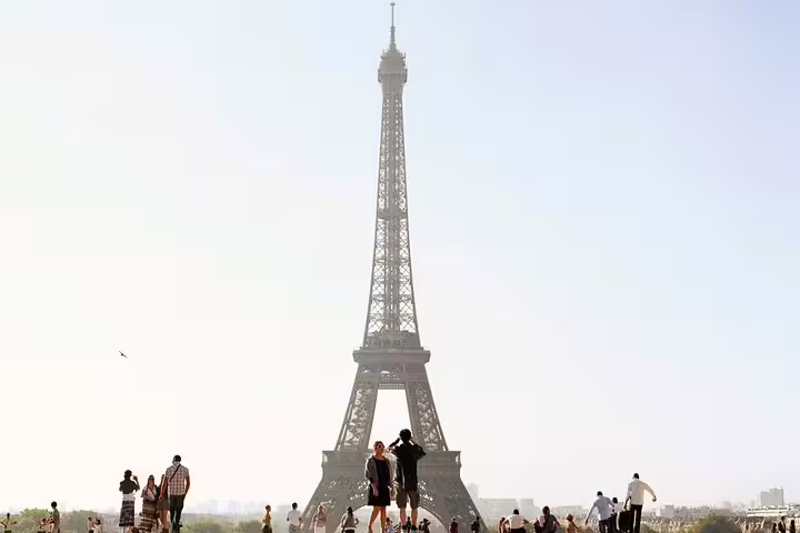 Tourists gathered at Trocadéro plaza with iconic Eiffel Tower rising against a hazy Paris sky