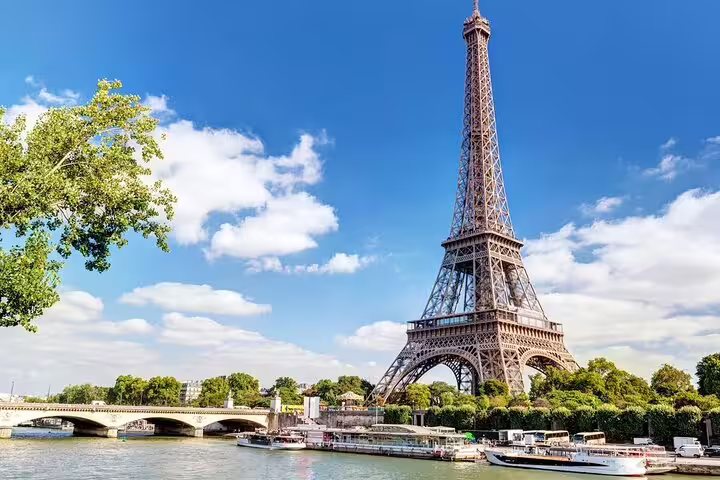 Eiffel Tower rising above the Seine River with boats and a bridge on a sunny day in Paris