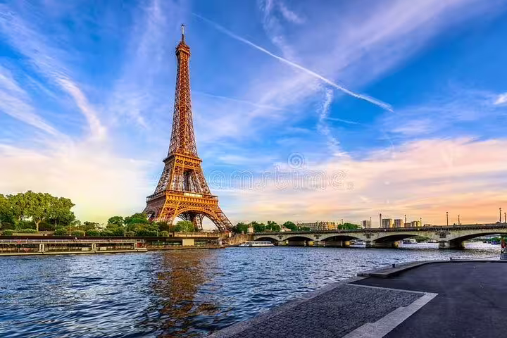 Eiffel Tower rising above the Seine River with a stone bridge and blue sky in Paris, France