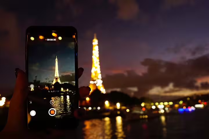 Smartphone recording the illuminated Eiffel Tower at night with the Seine River reflecting city lights in Paris